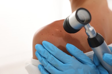 Photo of Doctor examining young woman's mole with dermatoscope on white background, closeup