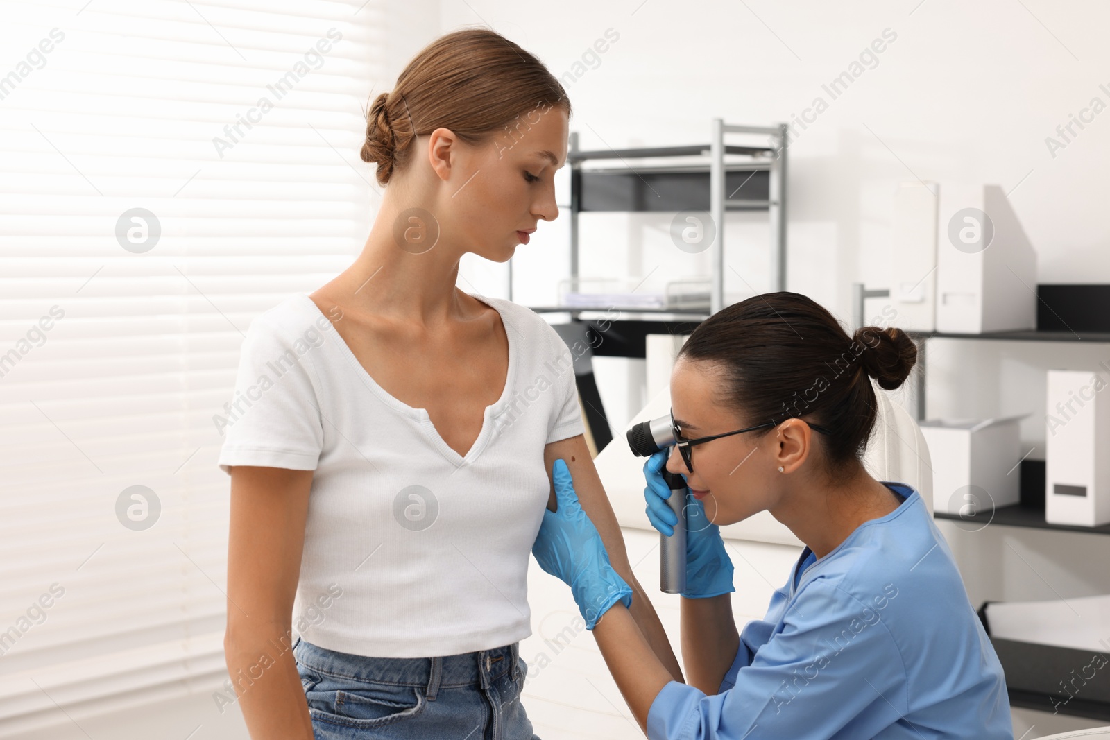 Doctor examining young woman's mole with dermatoscope in hospital Photo of Doctor examining young woman's mole with dermatoscope in hospital