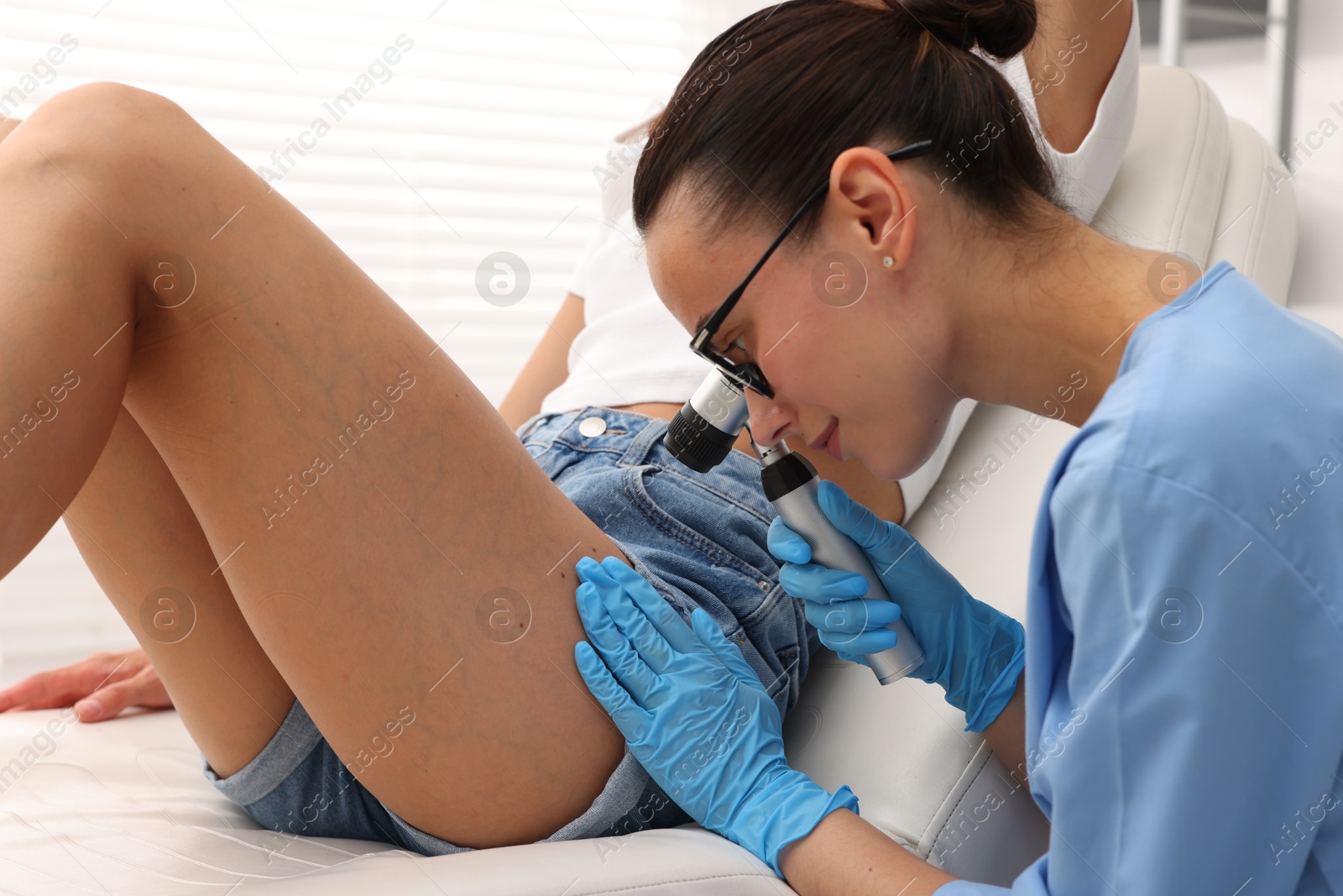 Doctor examining young woman's mole with dermatoscope in hospital Photo of Doctor examining young woman's mole with dermatoscope in hospital