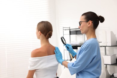 Photo of Doctor examining young woman's mole with magnifying glass in hospital