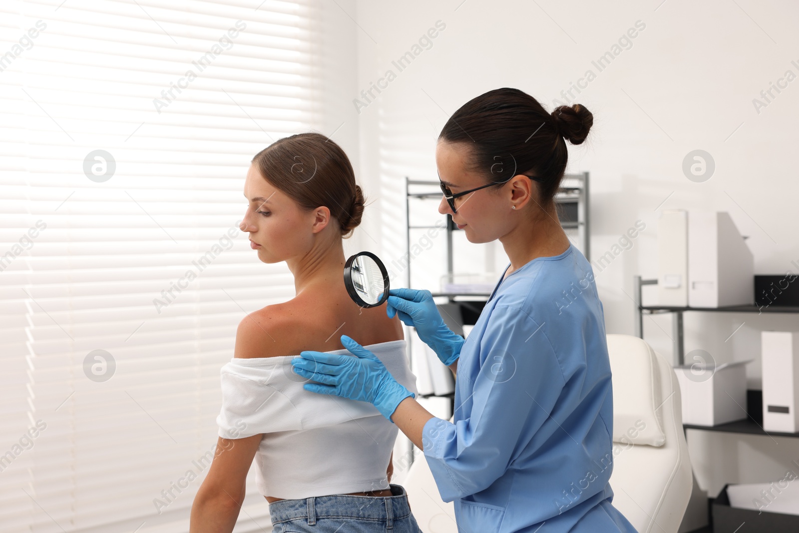Doctor examining young woman's mole with magnifying glass in hospital Photo of Doctor examining young woman's mole with magnifying glass in hospital