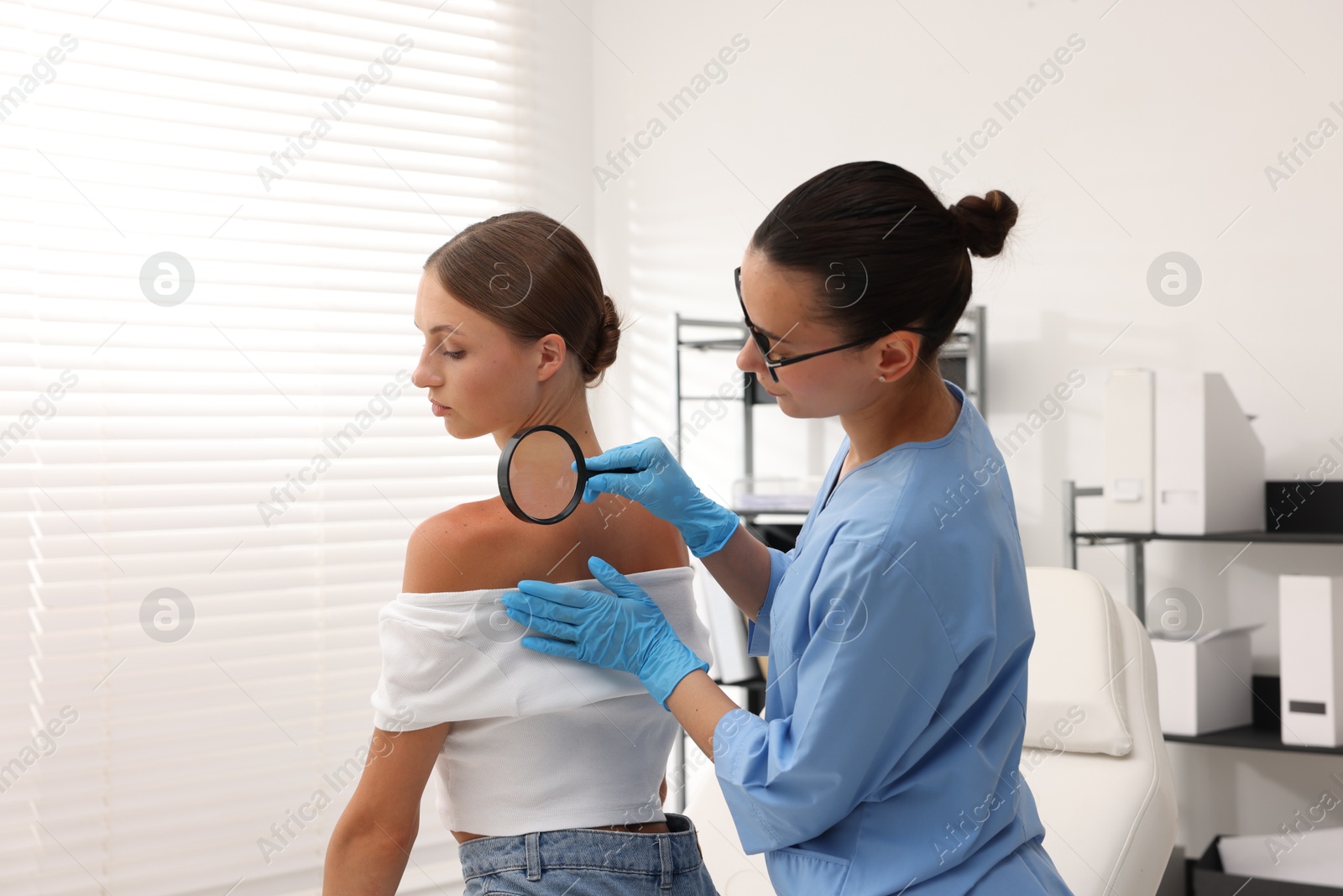 Doctor examining young woman's mole with magnifying glass in hospital Photo of Doctor examining young woman's mole with magnifying glass in hospital