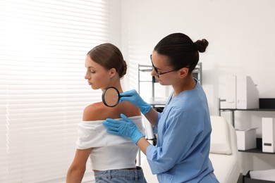 Photo of Doctor examining young woman's mole with magnifying glass in hospital