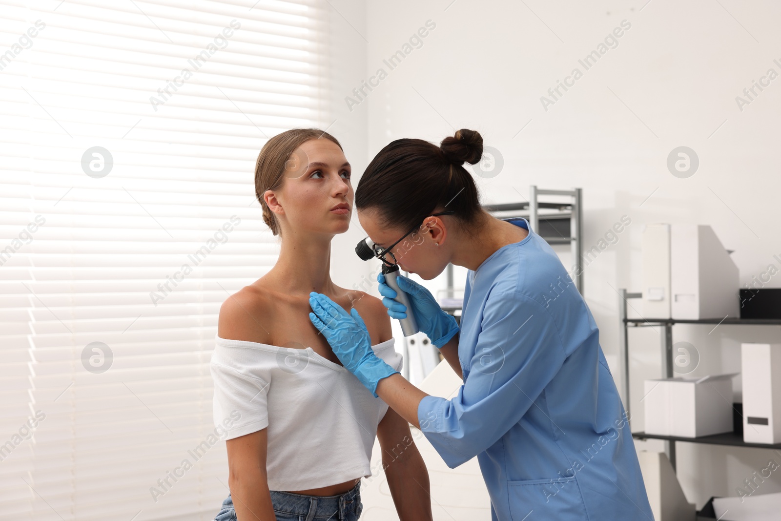Doctor examining young woman's mole with dermatoscope in hospital Photo of Doctor examining young woman's mole with dermatoscope in hospital