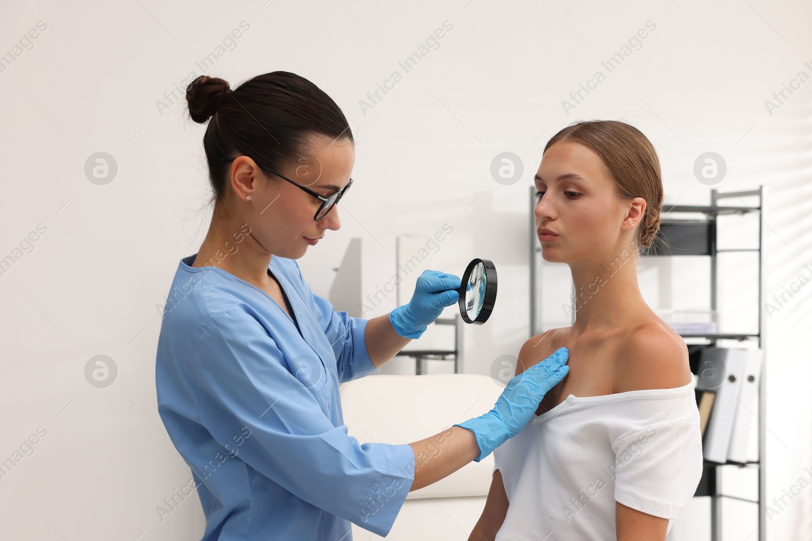 Doctor examining young woman's mole with magnifying glass in hospital Photo of Doctor examining young woman's mole with magnifying glass in hospital