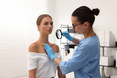 Photo of Doctor examining young woman's mole with magnifying glass in hospital
