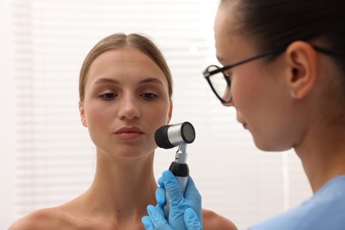Photo of Doctor examining young woman's mole with dermatoscope in hospital, closeup