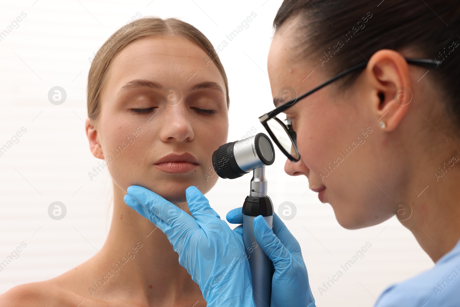 Doctor examining young woman's mole with dermatoscope in hospital, closeup Photo of Doctor examining young woman's mole with dermatoscope in hospital, closeup