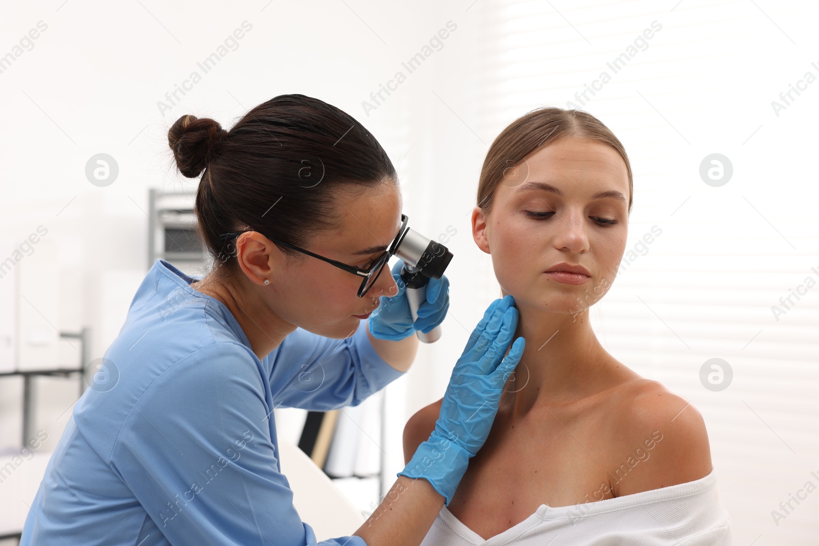 Doctor examining young woman's mole with dermatoscope in hospital Photo of Doctor examining young woman's mole with dermatoscope in hospital
