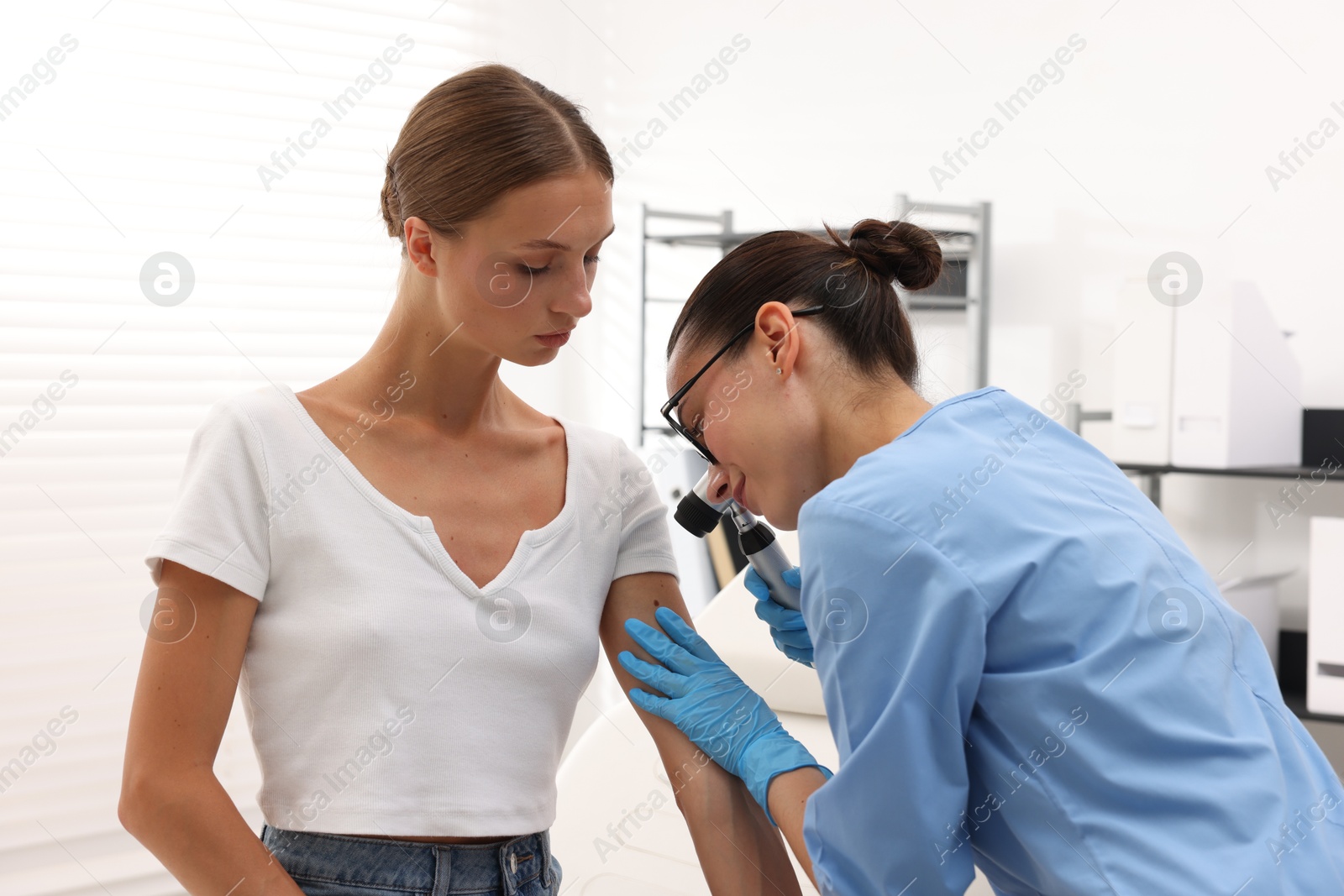 Doctor examining young woman's mole with dermatoscope in hospital Photo of Doctor examining young woman's mole with dermatoscope in hospital