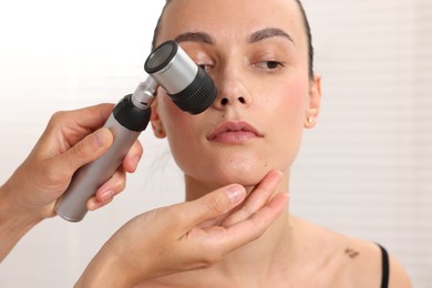 Photo of Doctor examining young woman's mole with dermatoscope in hospital, closeup