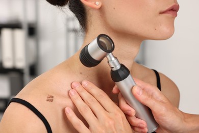 Photo of Doctor examining young woman's mole with dermatoscope in hospital, closeup