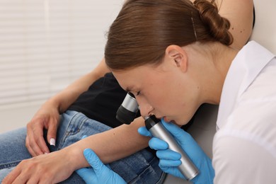 Photo of Doctor examining young woman's mole with dermatoscope in hospital, closeup