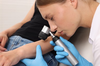 Photo of Doctor examining young woman's mole with dermatoscope in hospital, closeup