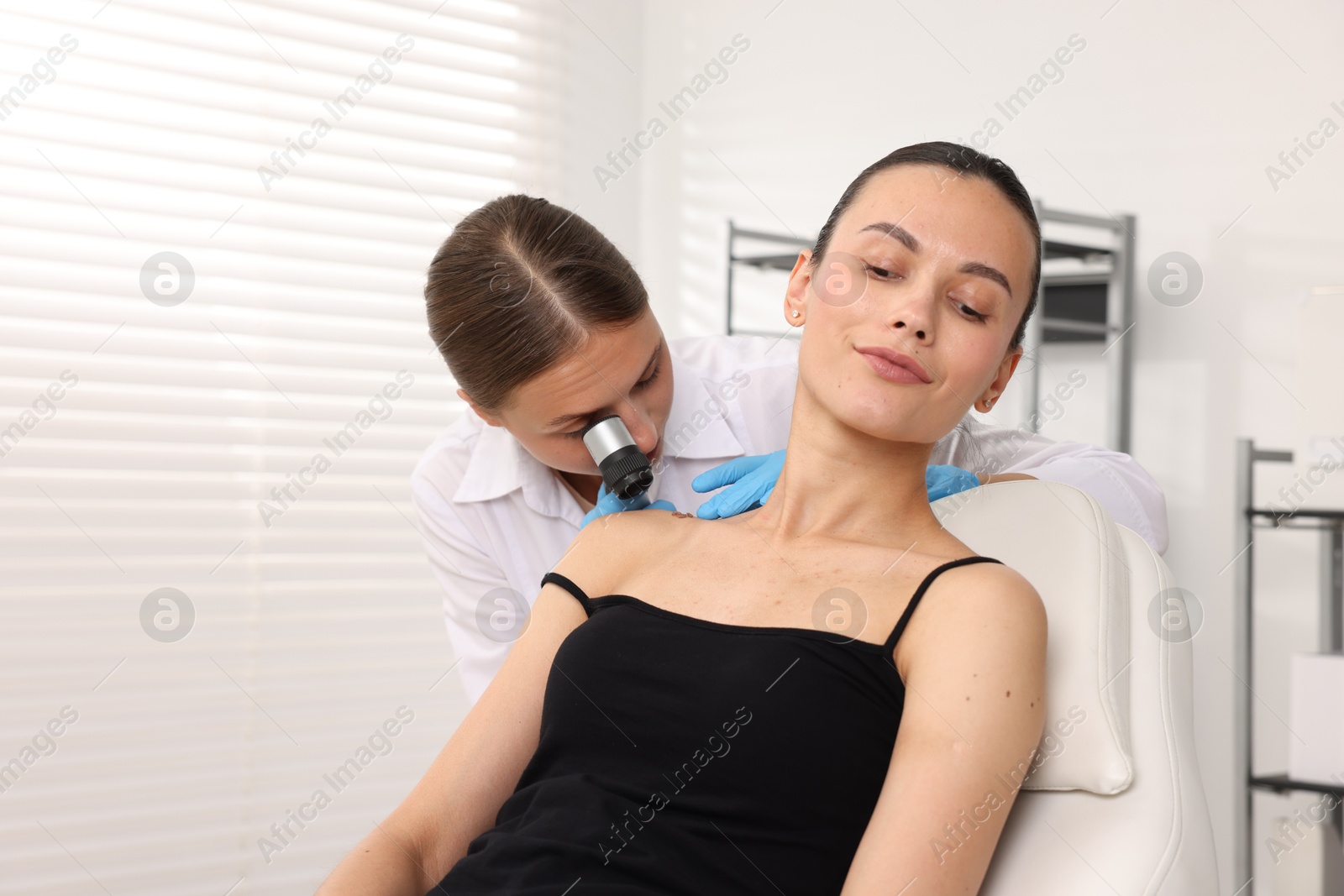 Doctor examining young woman's mole with dermatoscope in hospital Photo of Doctor examining young woman's mole with dermatoscope in hospital