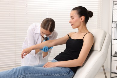 Photo of Doctor examining young woman's mole with dermatoscope in hospital