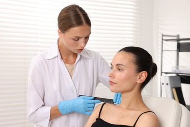 Photo of Doctor examining young woman's mole with ruler in hospital