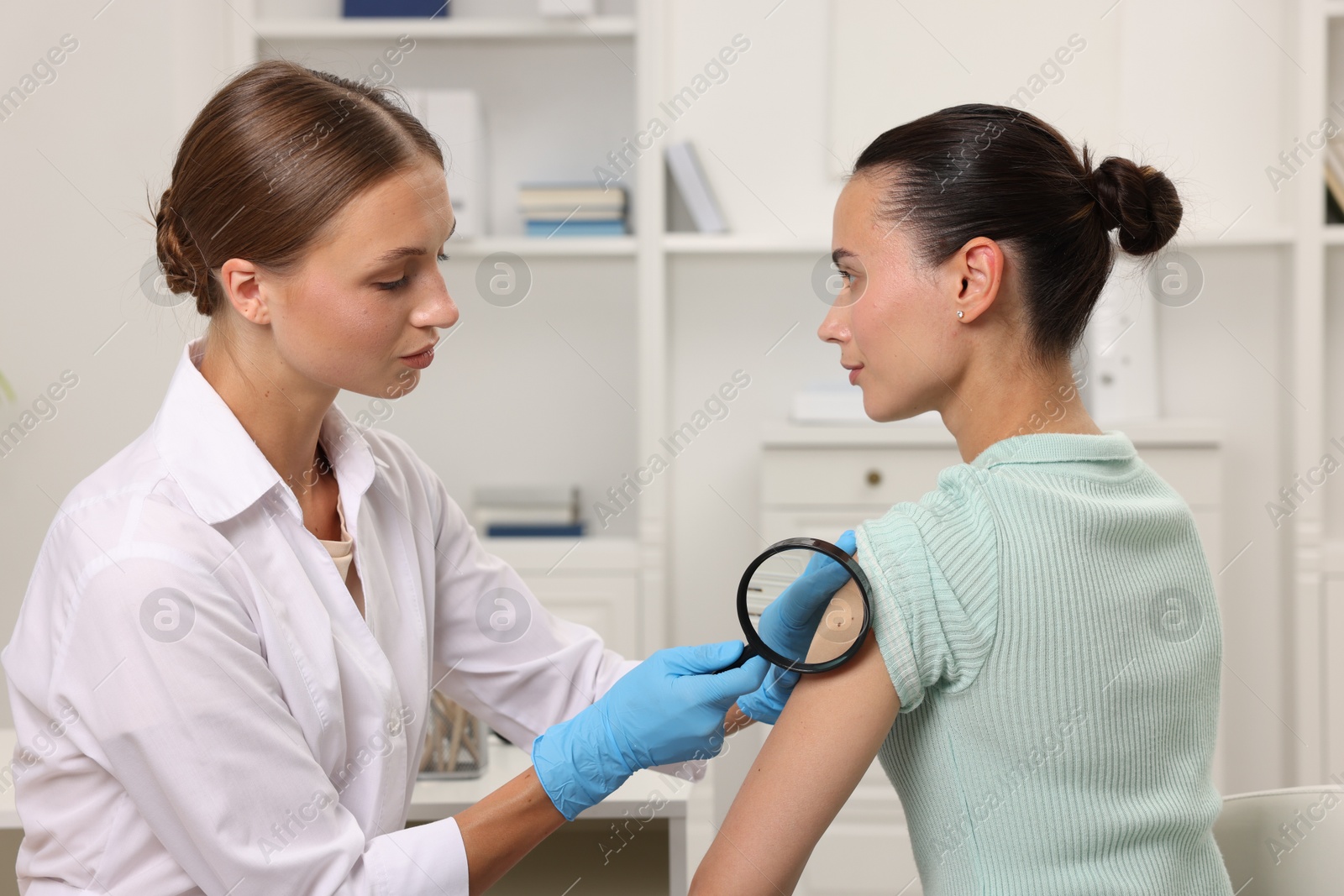 Photo of Doctor examining young woman's mole with magnifying glass in hospital