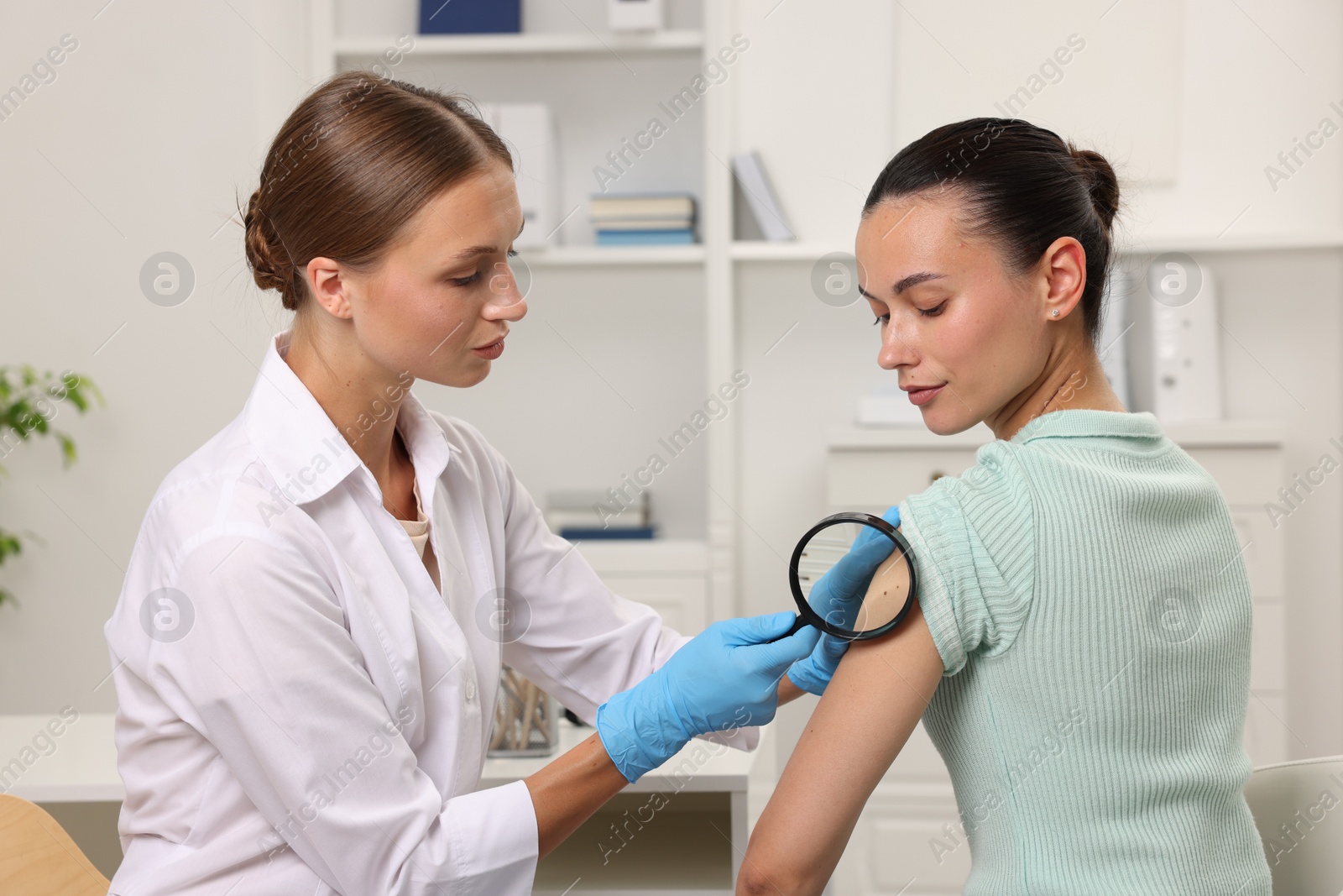 Photo of Doctor examining young woman's mole with magnifying glass in hospital