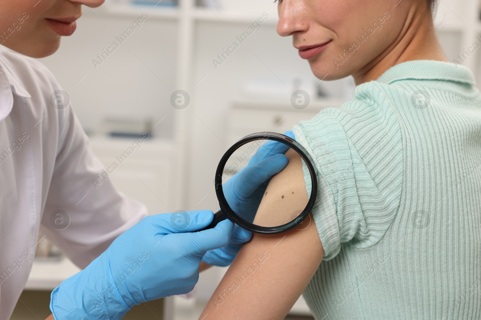 Photo of Doctor examining young woman's mole with magnifying glass in hospital, closeup