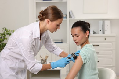 Photo of Doctor examining young woman's mole with dermatoscope in hospital