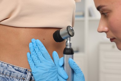 Photo of Doctor examining young woman's mole with dermatoscope in hospital, closeup
