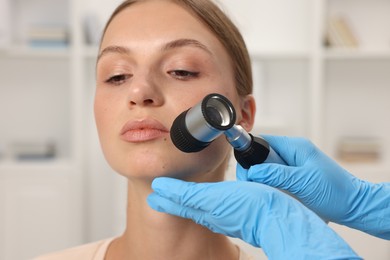 Photo of Doctor examining young woman's mole with dermatoscope in hospital, closeup
