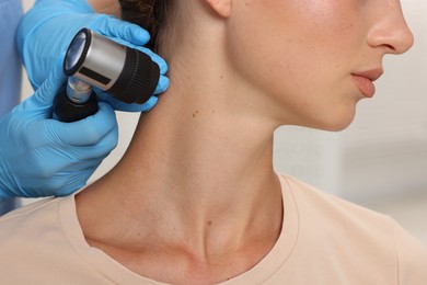 Photo of Doctor examining young woman's mole with dermatoscope in hospital, closeup