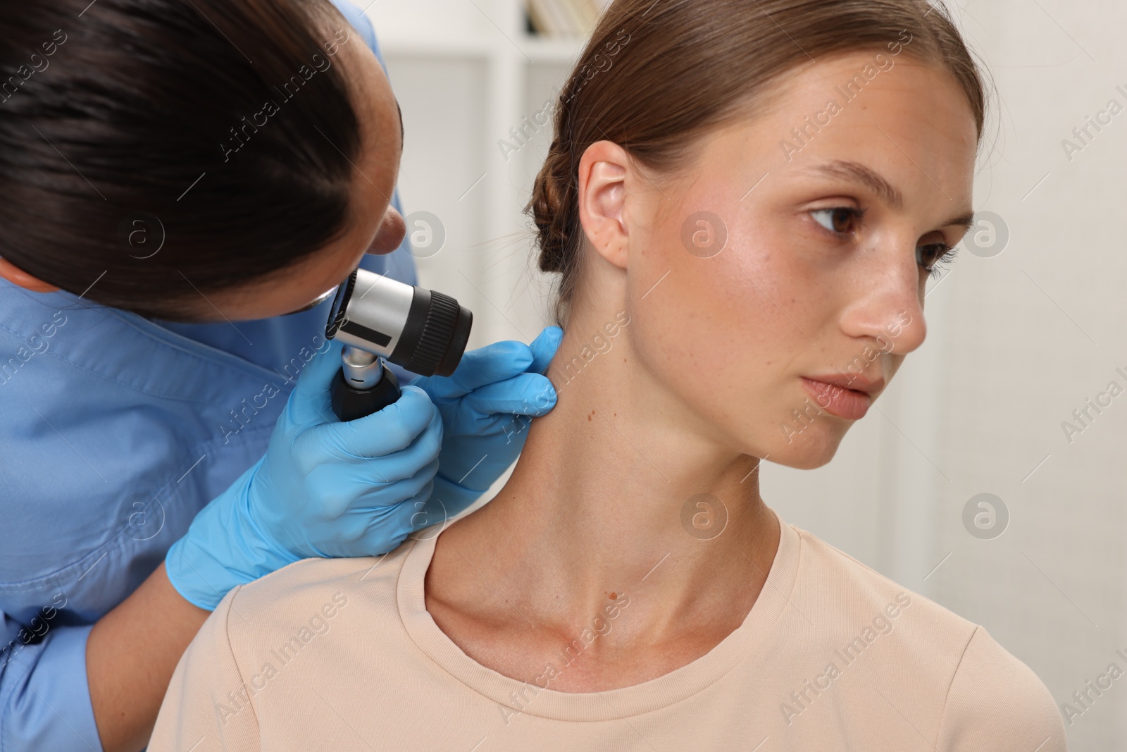 Photo of Doctor examining young woman's mole with dermatoscope in hospital, closeup