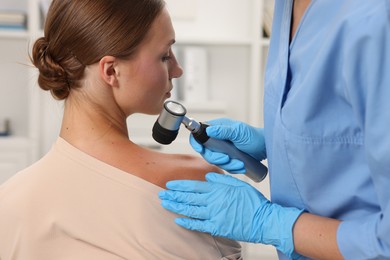 Photo of Doctor examining young woman's mole with dermatoscope in hospital, closeup