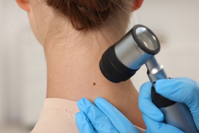 Photo of Doctor examining young woman's mole with dermatoscope in hospital, closeup