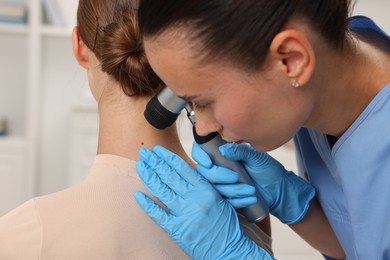 Photo of Doctor examining young woman's mole with dermatoscope in hospital, closeup