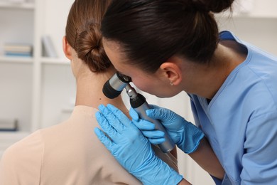 Photo of Doctor examining young woman's mole with dermatoscope in hospital, closeup