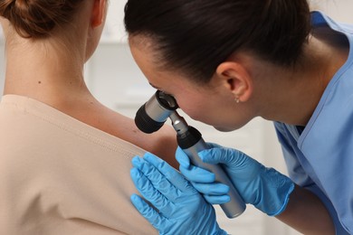 Photo of Doctor examining young woman's mole with dermatoscope in hospital, closeup