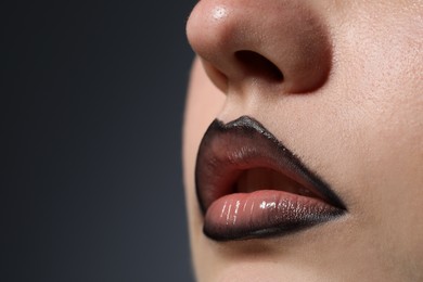 Photo of Beautiful young woman with black lip liner on dark grey background, closeup. Space for text