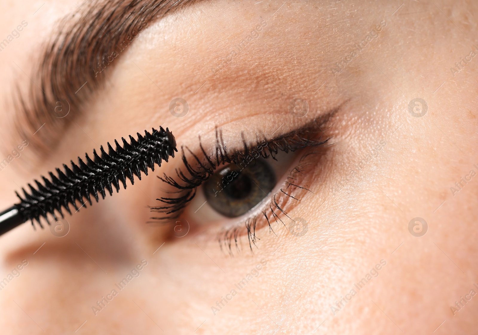 Young woman applying mascara onto her eyelashes, closeup Photo of Young woman applying mascara onto her eyelashes, closeup