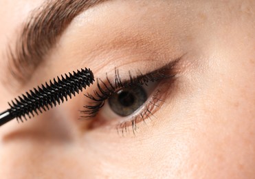 Photo of Young woman applying mascara onto her eyelashes, closeup