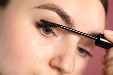 Photo of Young woman applying mascara onto her eyelashes on pink background, closeup