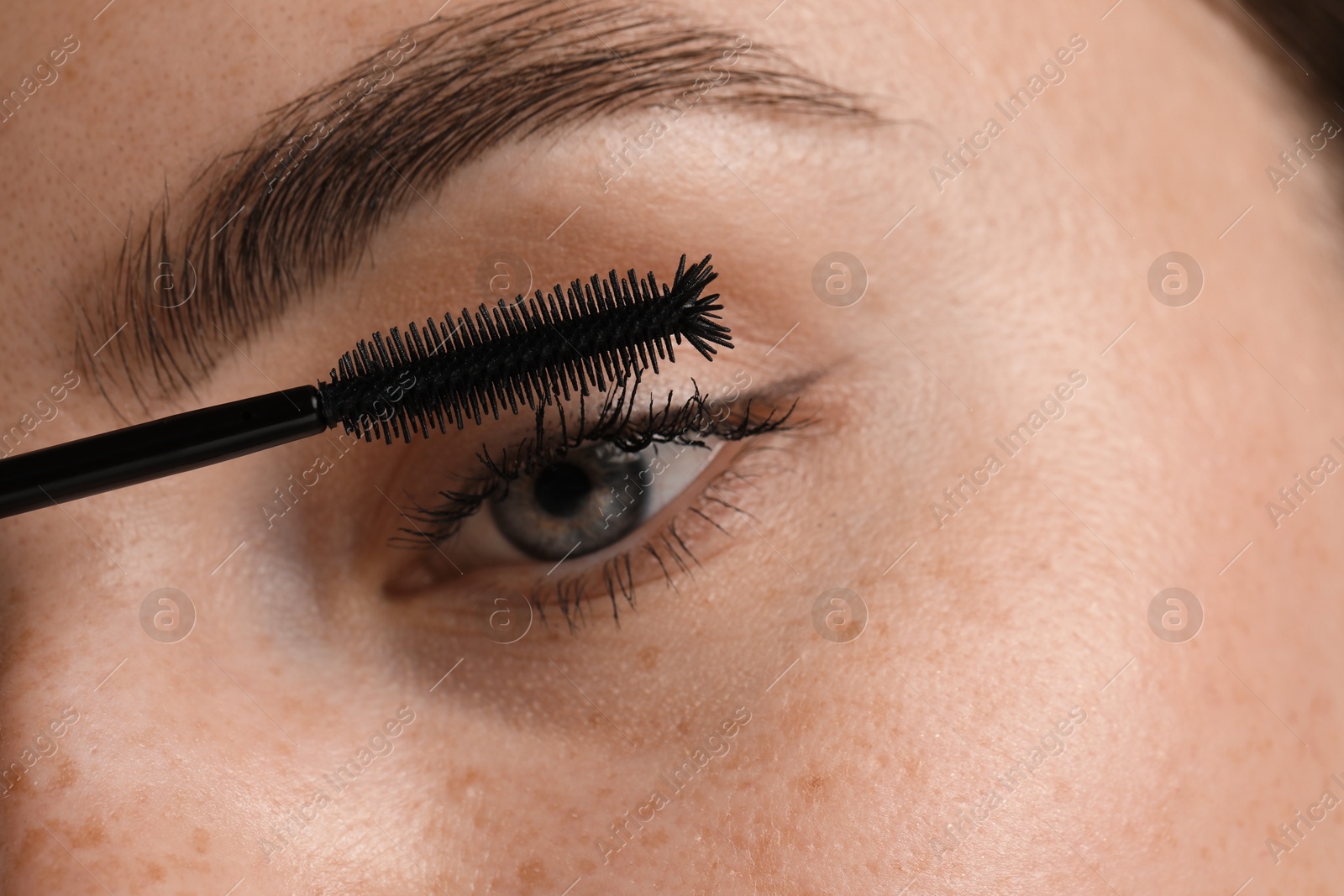 Young woman applying mascara onto her eyelashes, closeup Photo of Young woman applying mascara onto her eyelashes, closeup