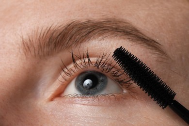 Photo of Young woman applying mascara onto her eyelashes, closeup