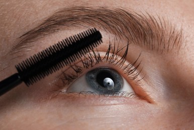 Photo of Young woman applying mascara onto her eyelashes, closeup
