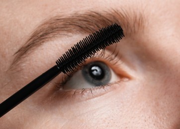 Photo of Young woman applying mascara onto her eyelashes, closeup