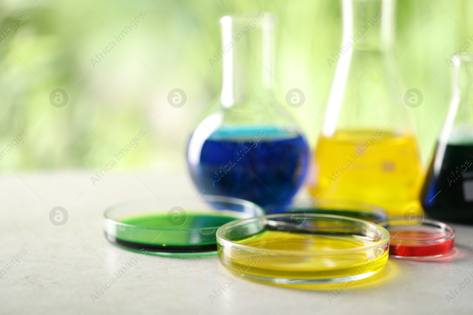 Photo of Laboratory glassware with different samples on light grey table outdoors, closeup. Solution chemistry