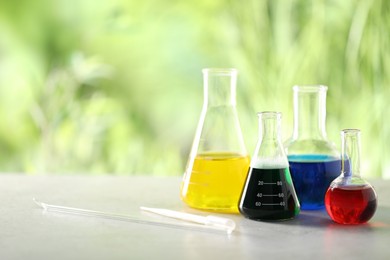 Photo of Solution chemistry. Laboratory glassware with different samples, pipette and stirring rod on light grey table outdoors, space for text