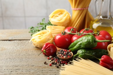 Photo of Different types of pasta and ingredients on wooden table, closeup. Space for text