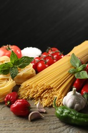 Photo of Different types of pasta and ingredients on wooden table, closeup