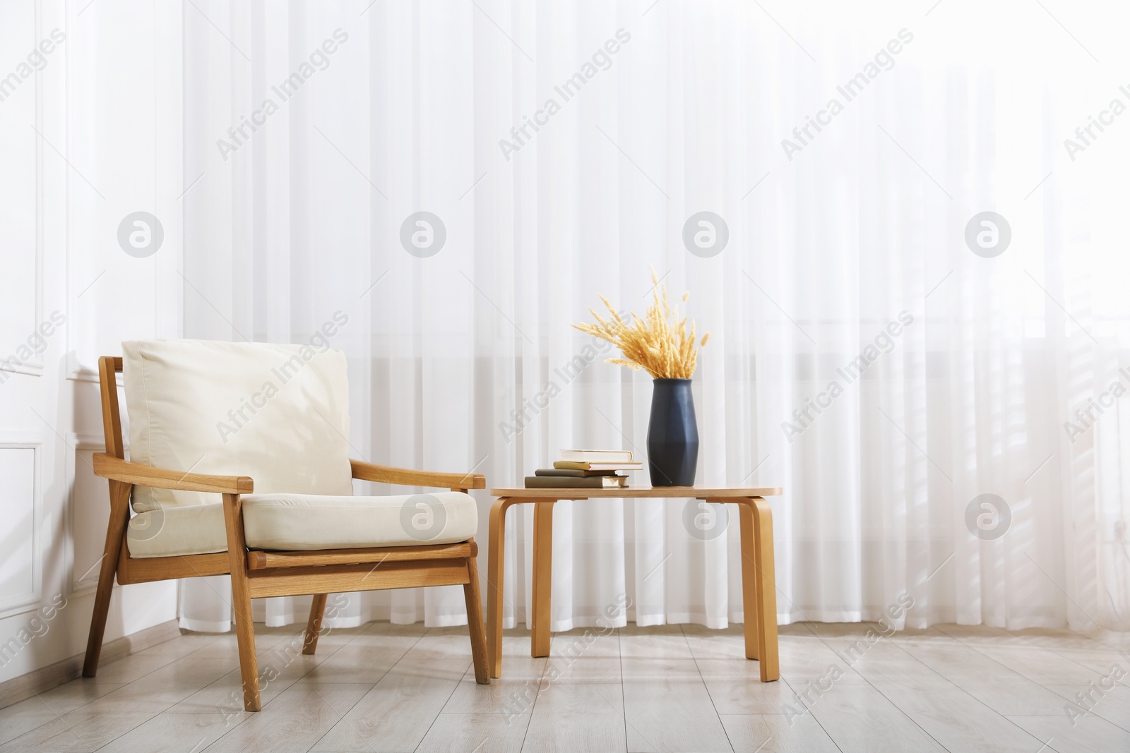 Comfortable beige armchair and table with vase and books near window indoors Photo of Comfortable beige armchair and table with vase and books near window indoors