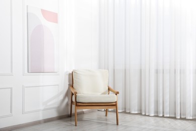 Photo of Comfortable beige armchair near window with curtains indoors