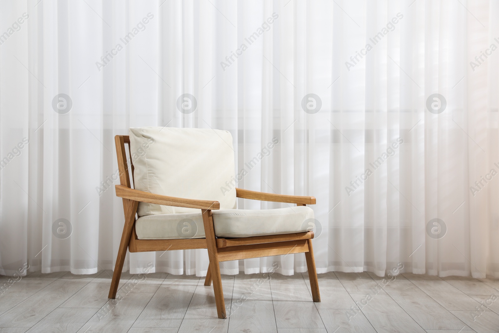Comfortable beige armchair near window with curtains indoors Photo of Comfortable beige armchair near window with curtains indoors