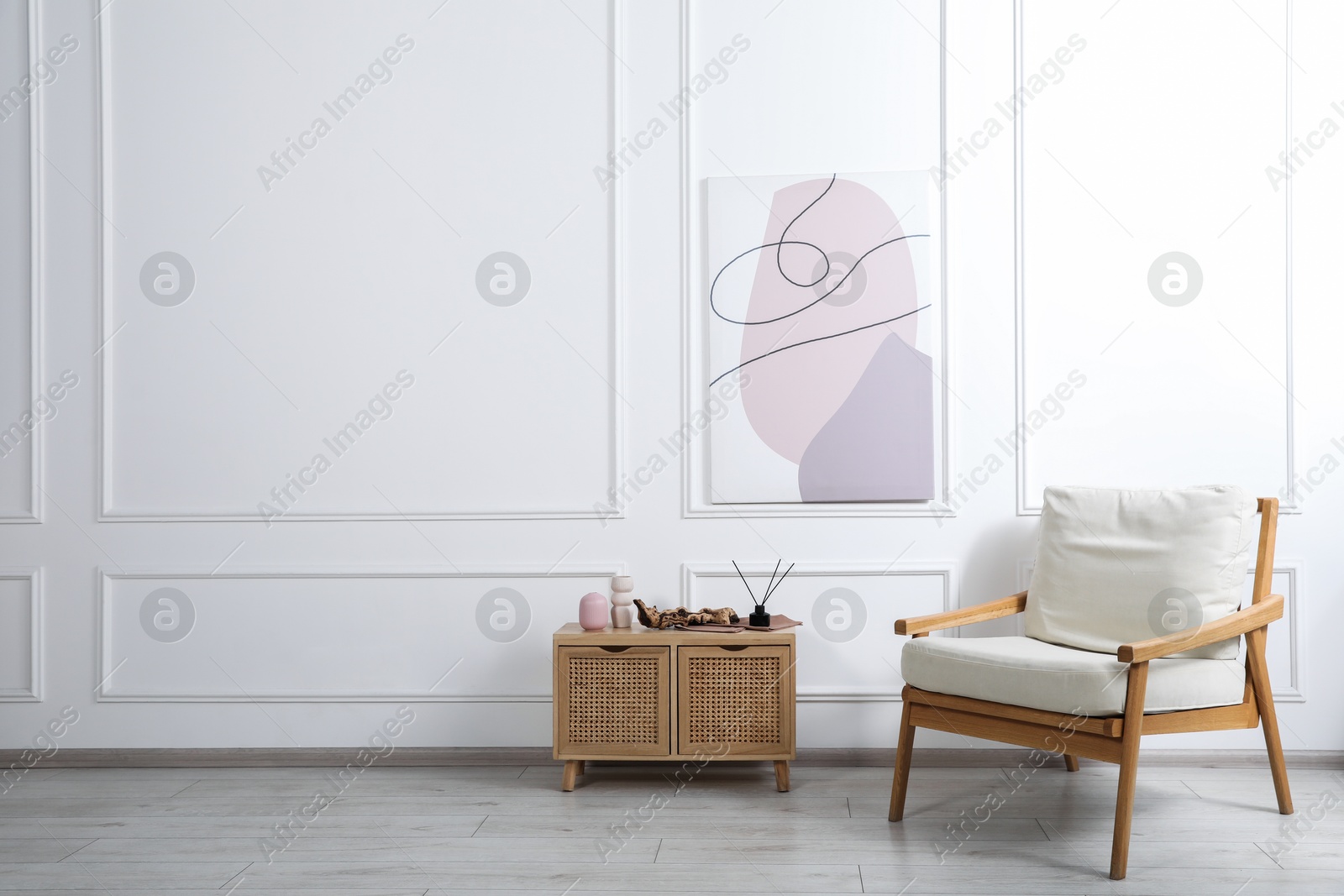 Comfortable beige armchair and wooden cabinet with decor near white wall indoors, space for text Photo of Comfortable beige armchair and wooden cabinet with decor near white wall indoors, space for text
